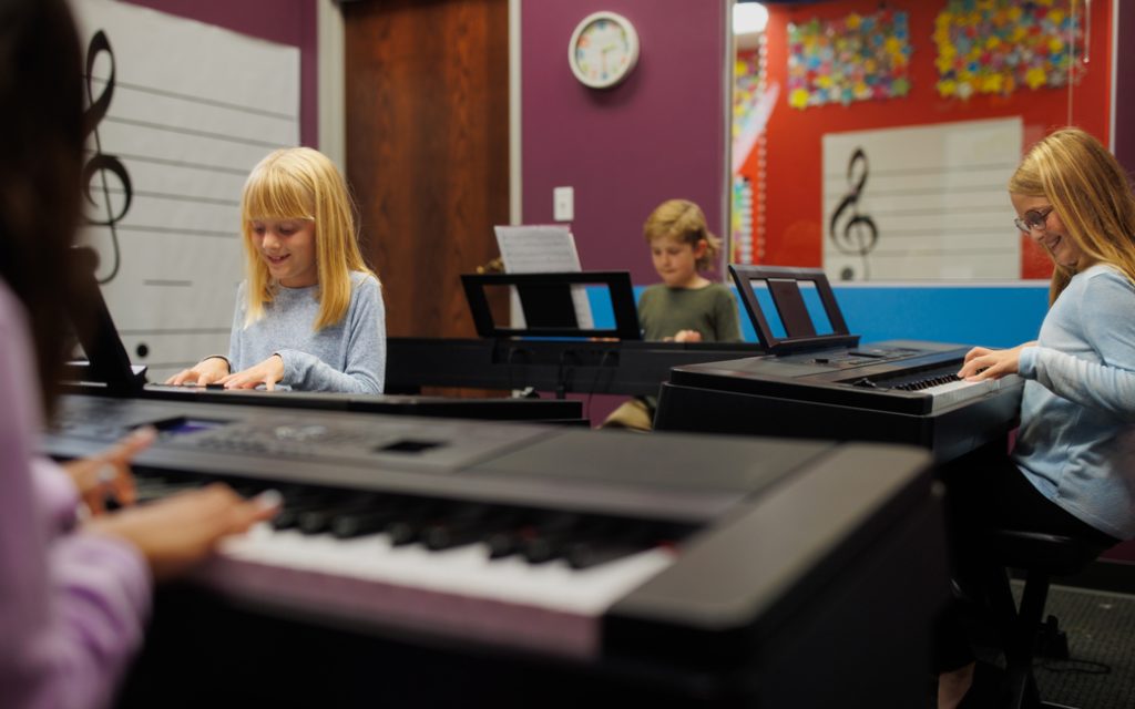 four students playing piano in classroom